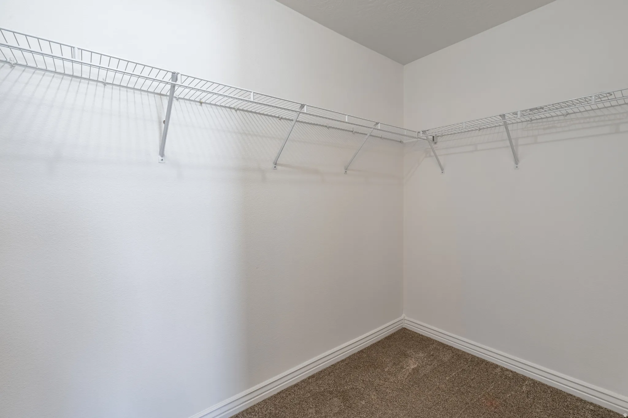 Corner closet featuring white wire shelving, light-colored walls, white baseboards, and brown carpet