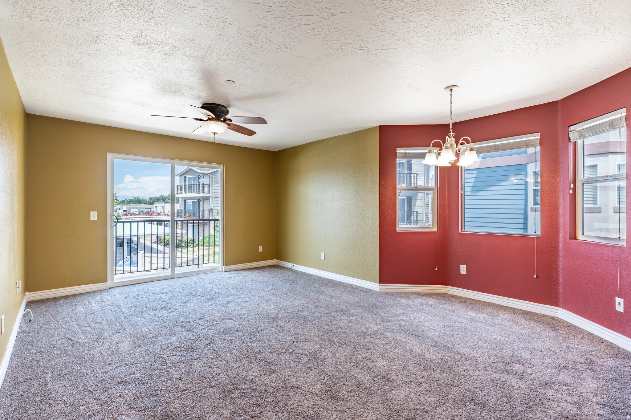 Spacious living area featuring neutral carpeting, a ceiling fan, and a sliding glass door opening to a balcony with black metal railings