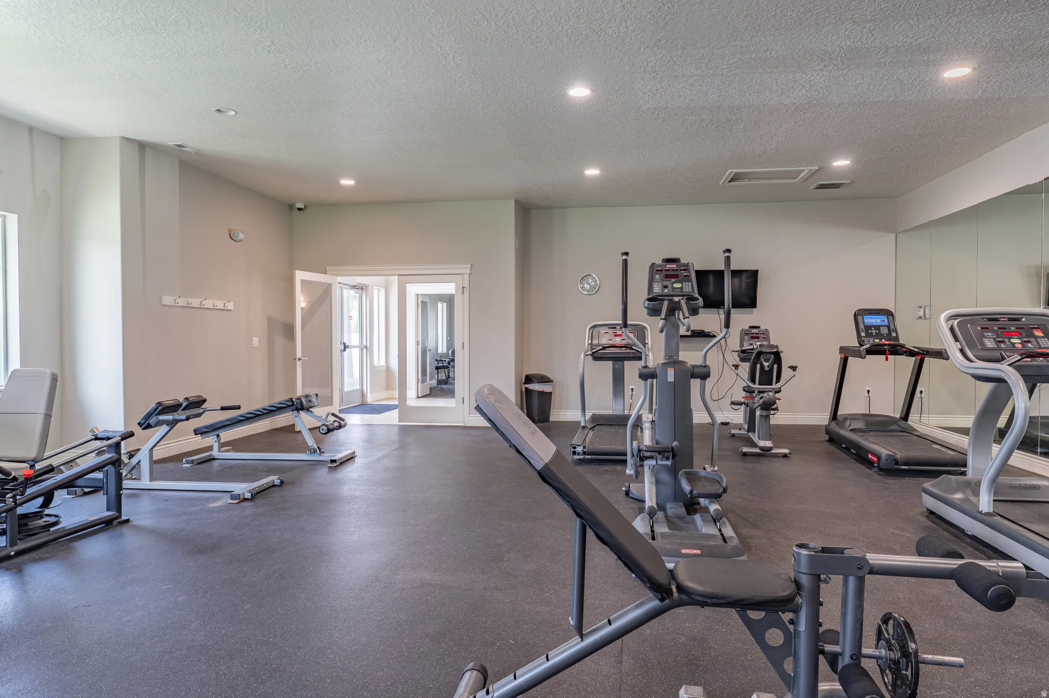 Dedicated fitness room featuring rubber flooring, recessed lighting, mirrored wall, and dual pane glass doors