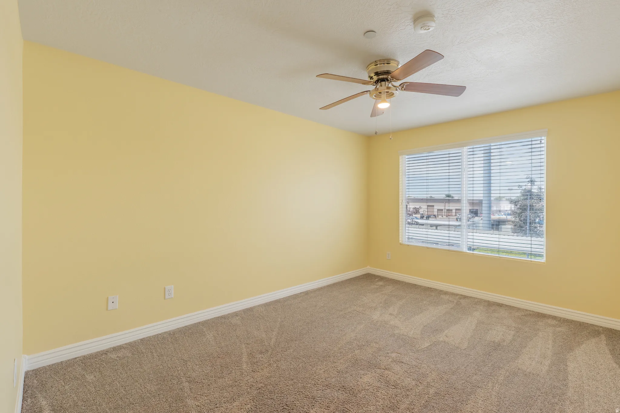 Carpeted room with a large window, ceiling fan, and baseboard molding