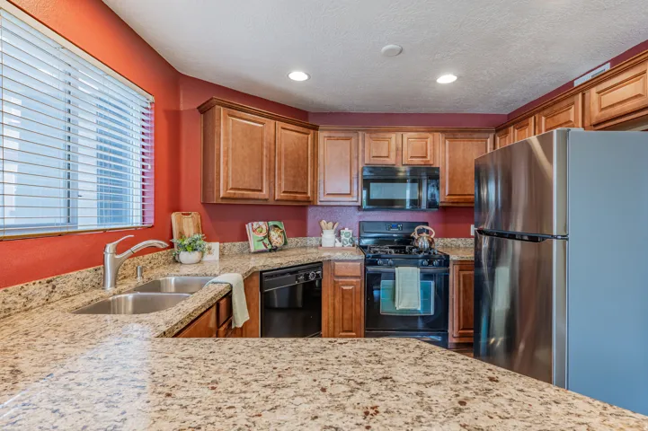 Kitchen featuring granite countertops, wood cabinetry, stainless steel refrigerator, black gas range, and built-in microwave