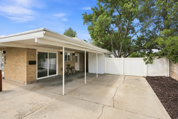 Brick exterior with covered carport, white vinyl fence, sliding glass door access, and paved driveway