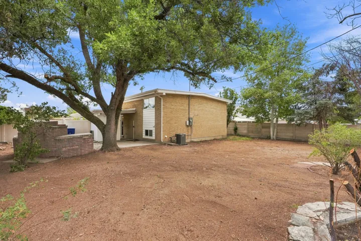 Expansive rear yard featuring a large mature tree, brick exterior, and a concrete patio