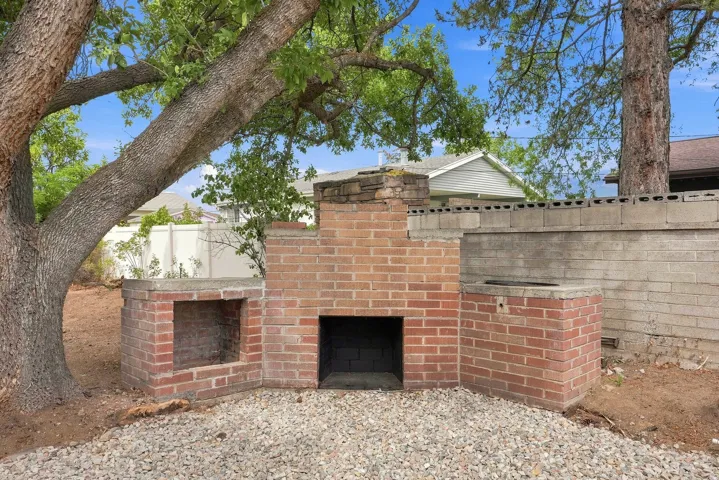 Outdoor brick fireplace with integrated storage, gravel ground cover, and a mature tree providing shade