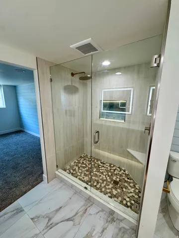 Spacious shower enclosure featuring a glass door, light-toned wall tiling, and a pebble-tiled floor
