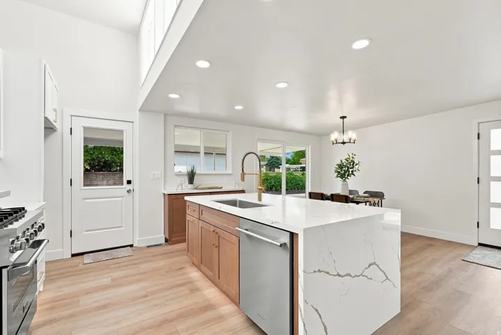 Open-concept kitchen featuring a waterfall island with a stone countertop, wood-finish flooring, recessed lighting, stainless steel appliances, and a vaulted ceiling with clerestory windows