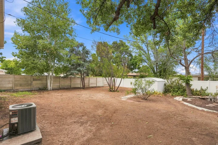 Expansive outdoor space featuring a combination of wood-panel and white vinyl fencing, a stone pathway, mature trees, and a detached storage shed
