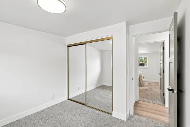 Carpeted room featuring a ceiling-mounted light fixture, mirrored sliding closet doors with gold-tone frames, white baseboards, and white walls