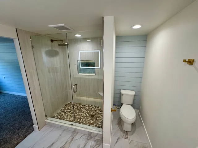 Glass-enclosed shower with pebble-tiled floor and a rain shower head