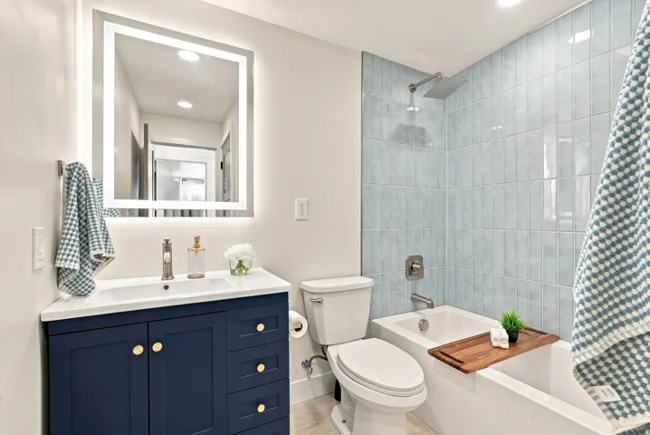 Bathroom featuring a deep blue vanity with gold-tone hardware, a white countertop with integrated sink, and an illuminated mirror