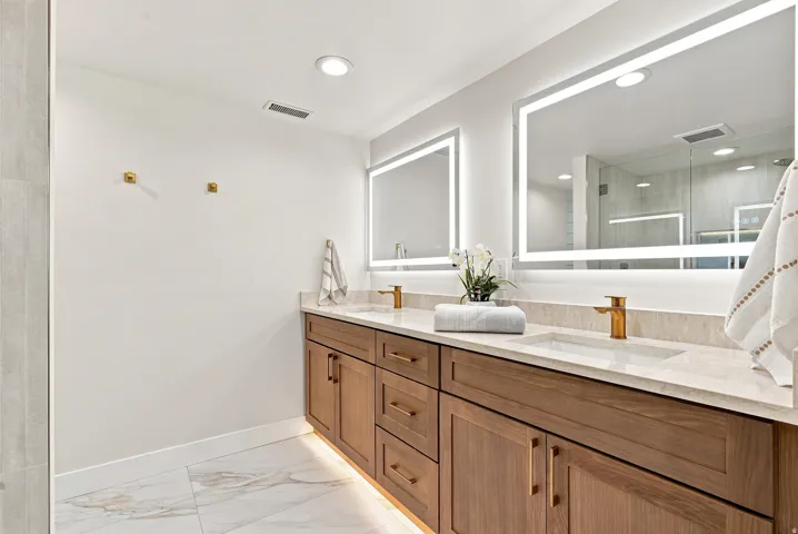 Dual vanity featuring integrated sinks, light-toned countertops, and wood-finish cabinetry with brass-toned hardware