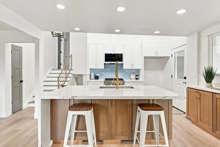 Kitchen featuring a large island with a waterfall countertop, white upper cabinetry, natural wood-finish lower cabinetry, and a blue subway tile backsplash