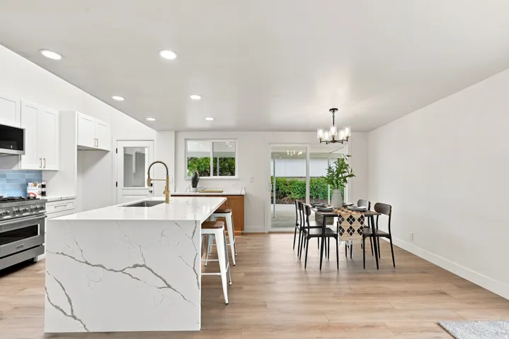 Spacious open-concept kitchen and dining area featuring a large island with waterfall countertop, stainless steel appliances, light wood-finish flooring, and recessed lighting