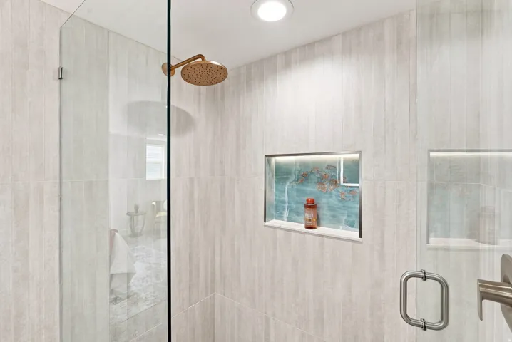 Walk-in shower featuring a frameless glass enclosure, a ceiling-mounted bronze-finish shower head, and light-toned vertical tile work
