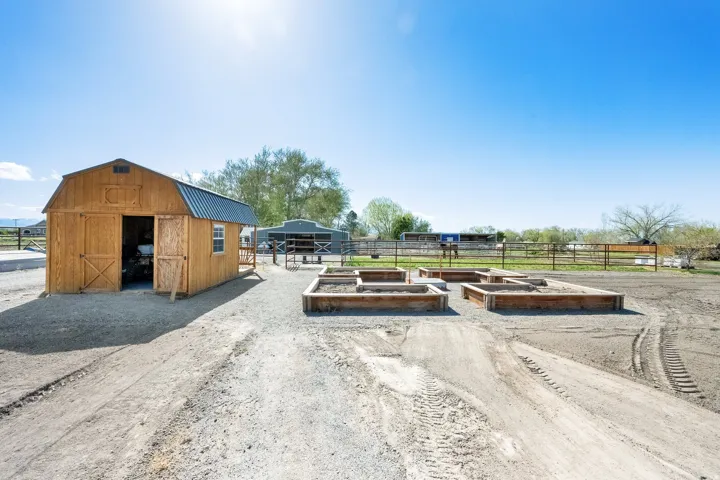 Freestanding wood-sided shed with a metal roof, multiple raised garden beds, and fenced perimeter
