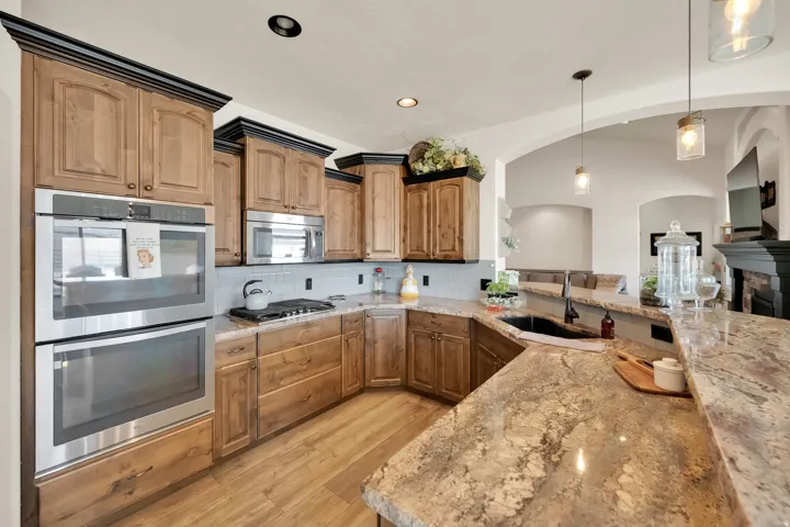 Gourmet kitchen featuring wood cabinetry, stainless steel double ovens, a gas range, a dark composite sink, and granite countertops