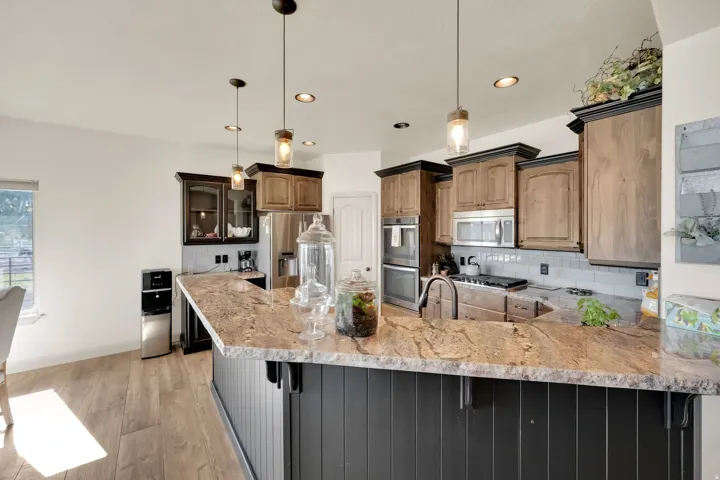 Spacious kitchen featuring a large island with stone countertops and beadboard paneling, stainless steel appliances, custom cabinetry with crown molding, a subway tile backsplash, and wood-finish flooring