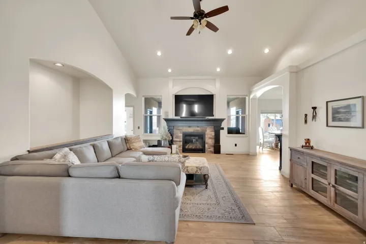 Spacious living area featuring light wood-finish flooring, a stone-front fireplace with a dark mantel, and recessed lighting