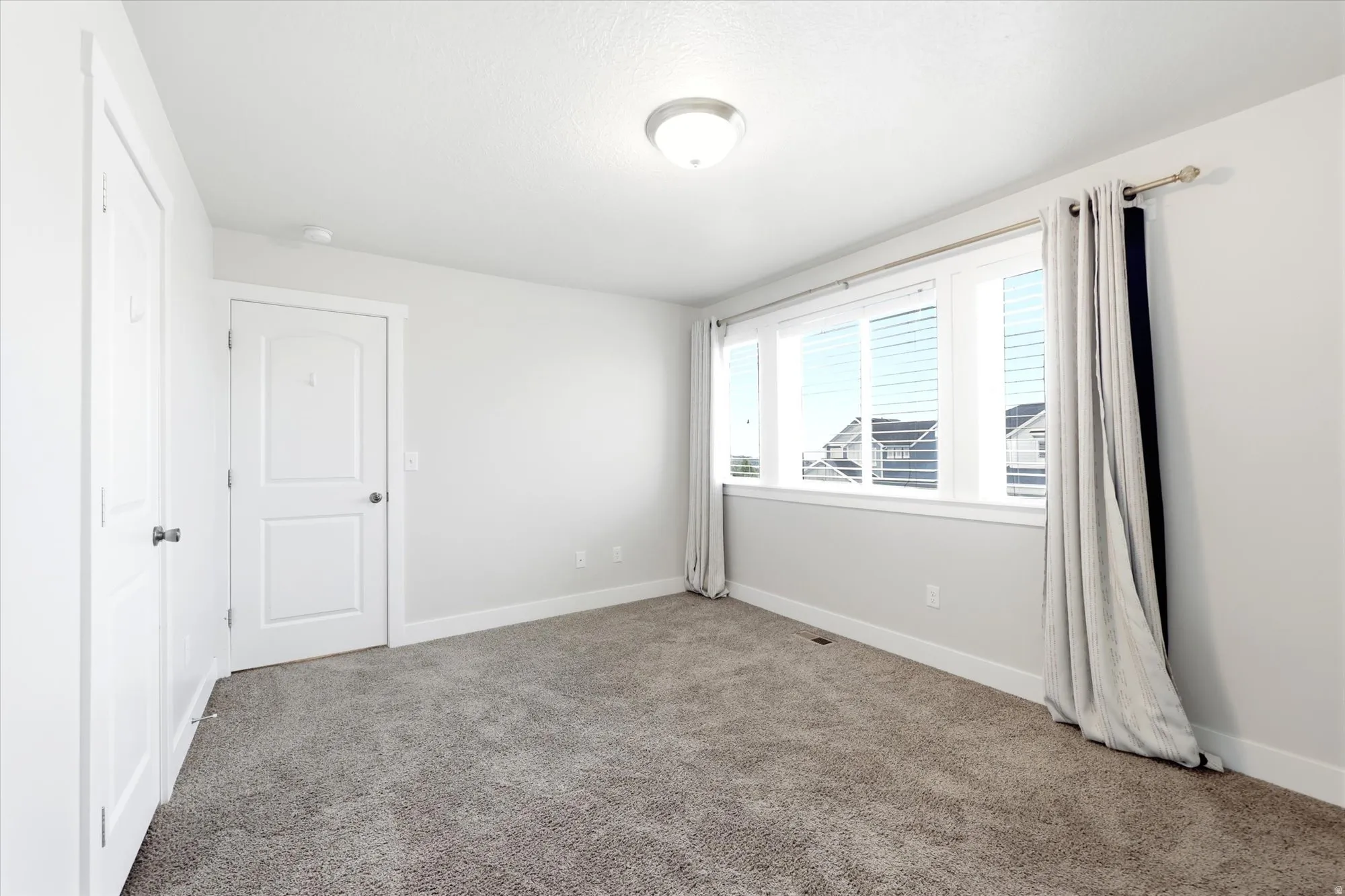 Bright room featuring a large window with horizontal blinds, neutral carpet, white trim, and a flush-mount ceiling light