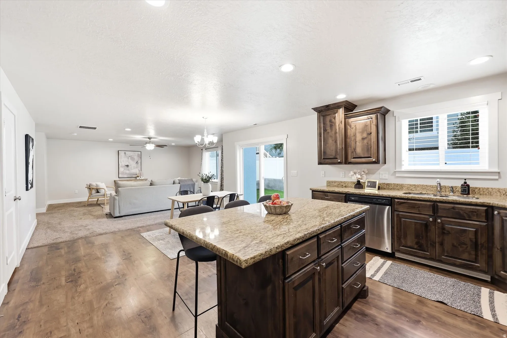 Kitchen island with stone-finish countertop, stainless steel appliances, dark wood-finish cabinetry, and wood-finish flooring