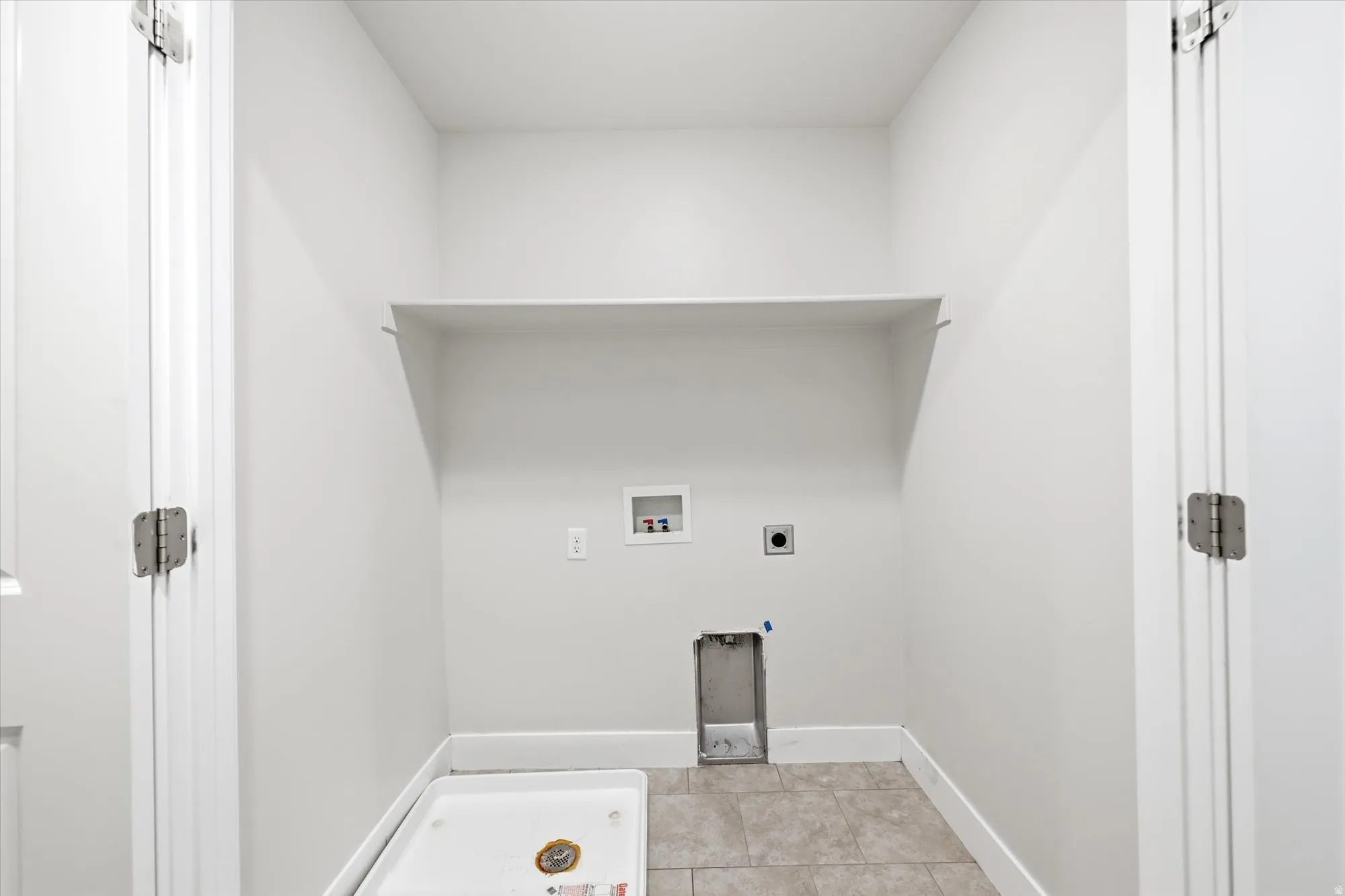 Dedicated utility space featuring a built-in shelf, plumbing hookups, and tiled flooring