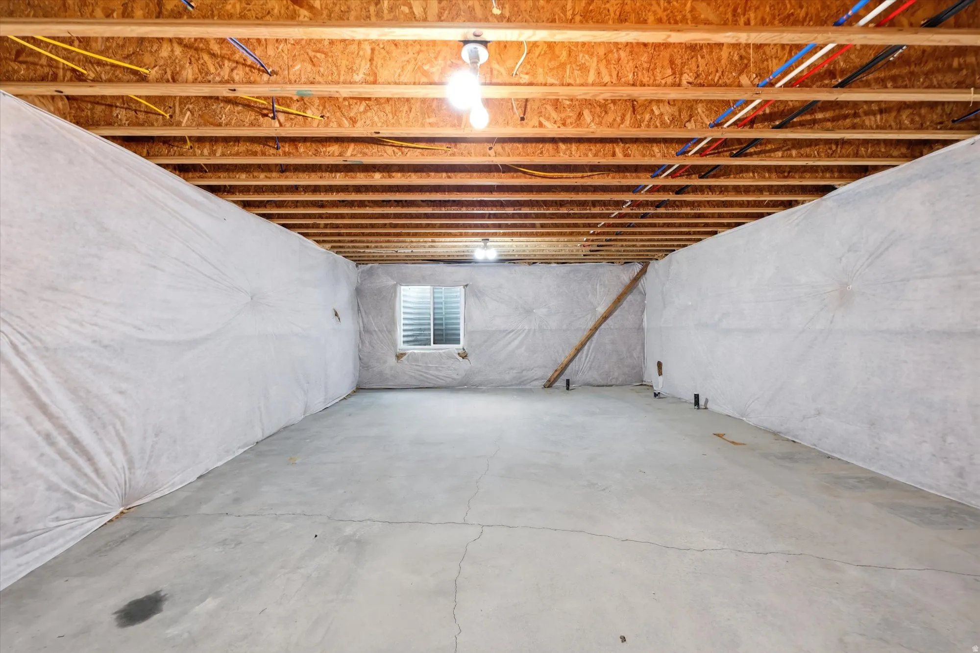 Unfinished basement with exposed wood joists and subfloor, concrete flooring, and insulated perimeter walls