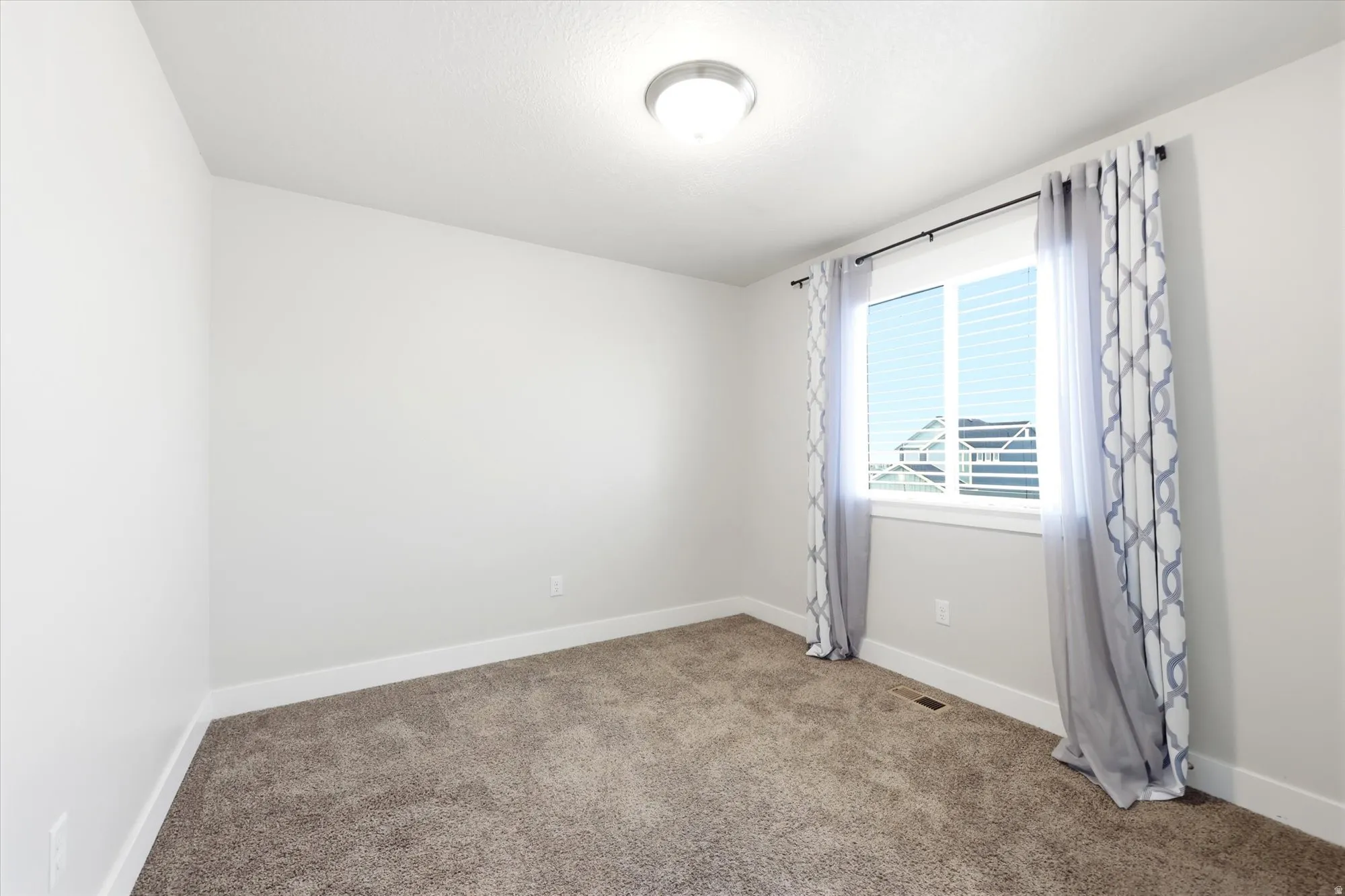 Office or bedroom. Carpeted room featuring a white-framed window with blinds, light gray walls, and a flush-mount ceiling light fixture