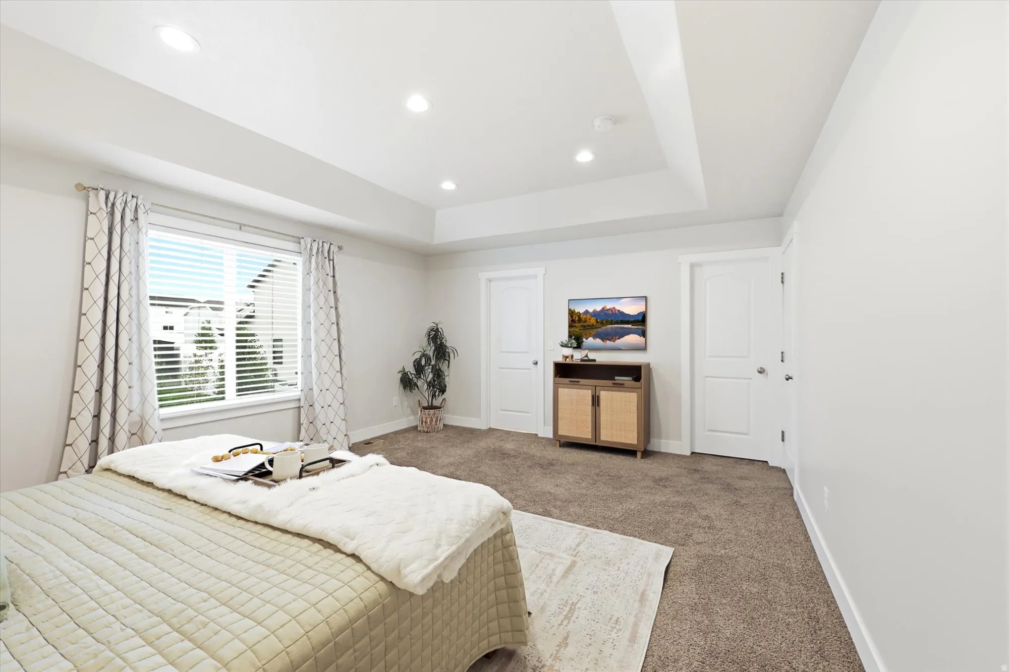 Spacious room featuring a tray ceiling with recessed lighting, a large window with blinds, and neutral carpeting