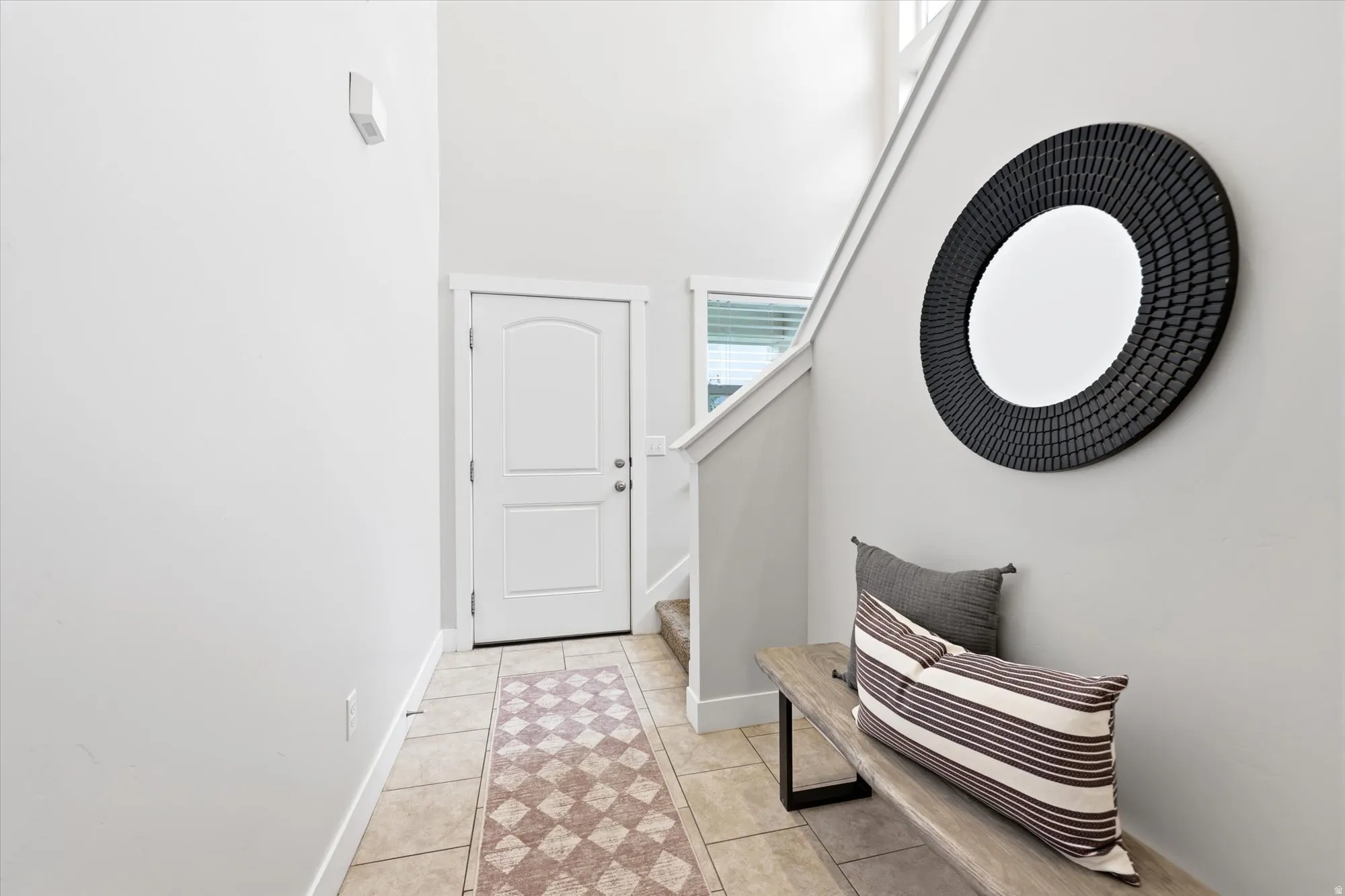 Bright entry foyer featuring tile flooring, a two-panel entry door, and a staircase with white balusters