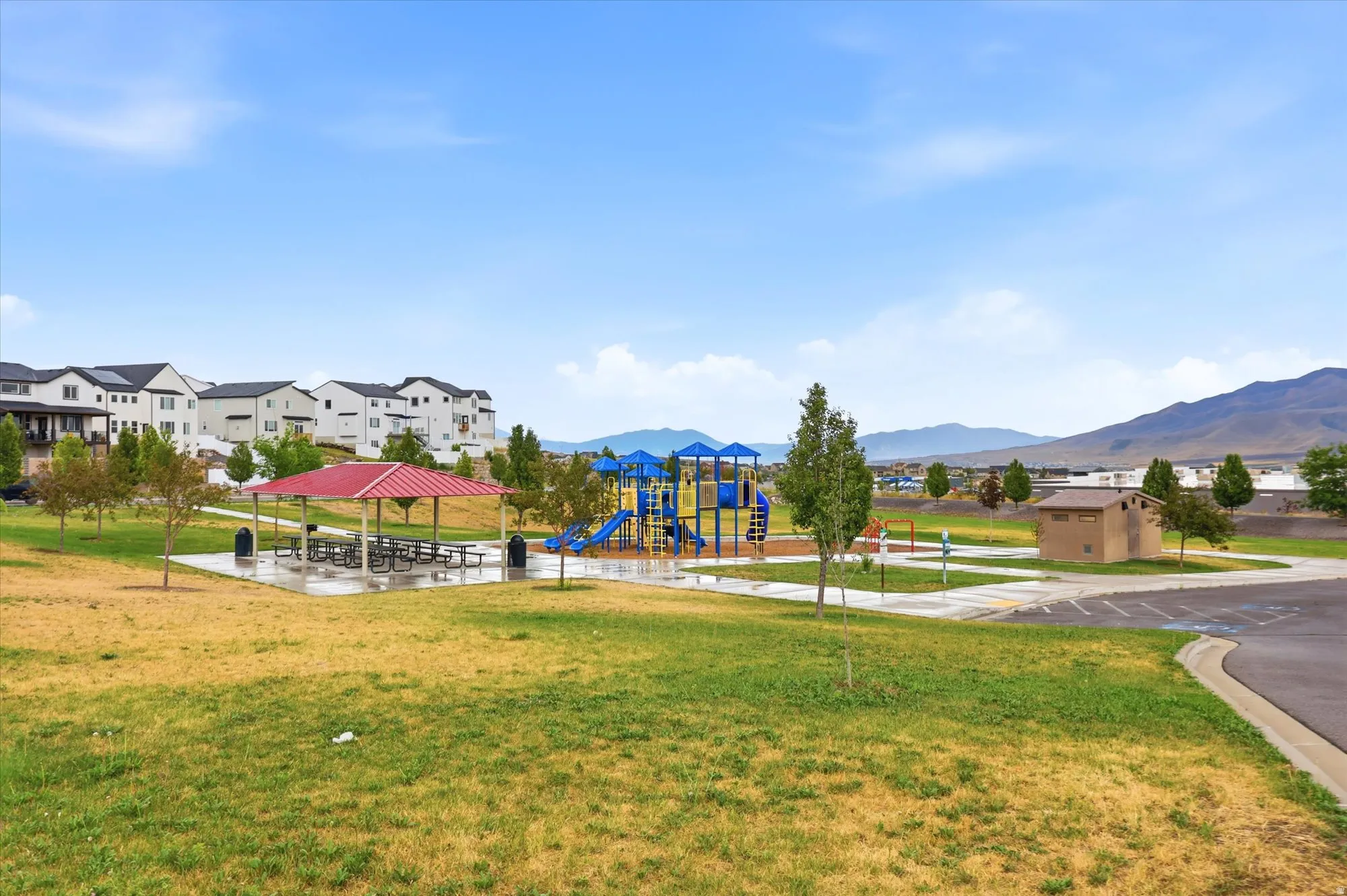 Community park featuring a covered picnic area, playground equipment, and paved walking paths