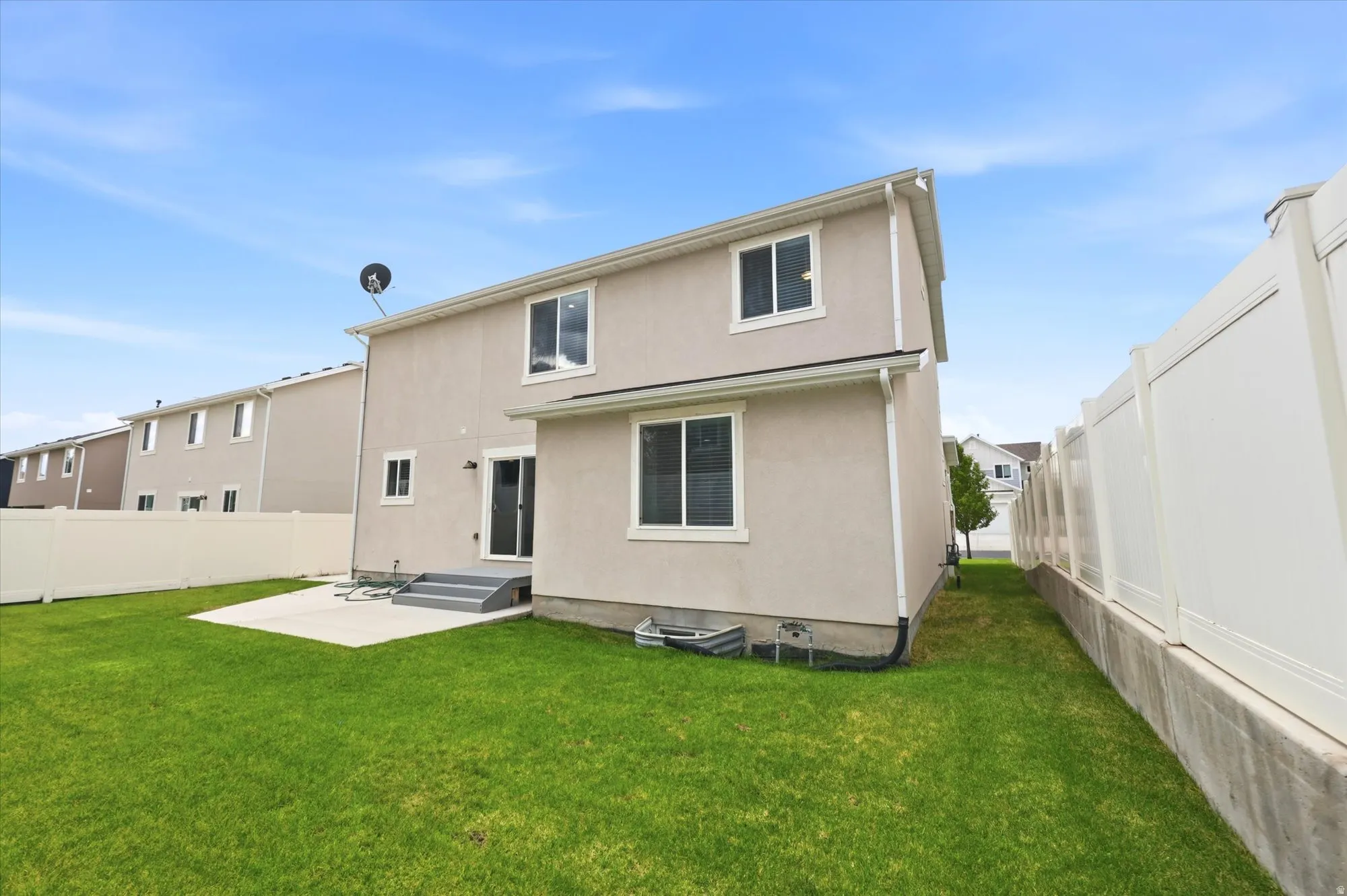 Expansive backyard featuring a manicured lawn, a concrete patio, and a white vinyl privacy fence