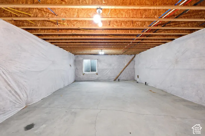 Unfinished basement with exposed wood joists and subfloor, concrete flooring, and insulated perimeter walls