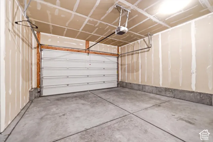 Attached garage featuring a concrete floor, automatic door opener, and unfinished drywall walls
