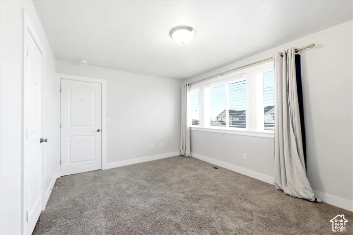 Bright room featuring a large window with horizontal blinds, neutral carpet, white trim, and a flush-mount ceiling light