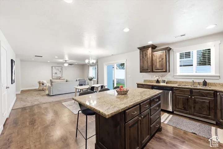 Kitchen island with stone-finish countertop, stainless steel appliances, dark wood-finish cabinetry, and wood-finish flooring