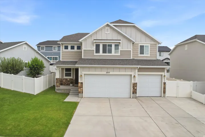 Modern two-story residence featuring a two-car garage, stone accents on the facade, a concrete driveway, and a white vinyl fence enclosing a green lawn