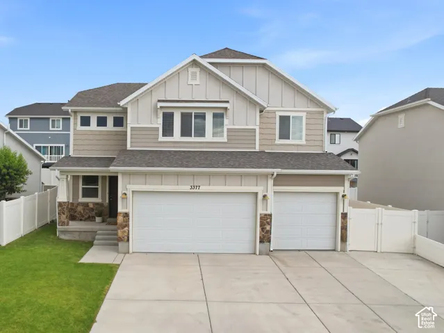 Modern two-story residence featuring a two-car garage, stone accents on the facade, a concrete driveway, and a white vinyl fence enclosing a green lawn