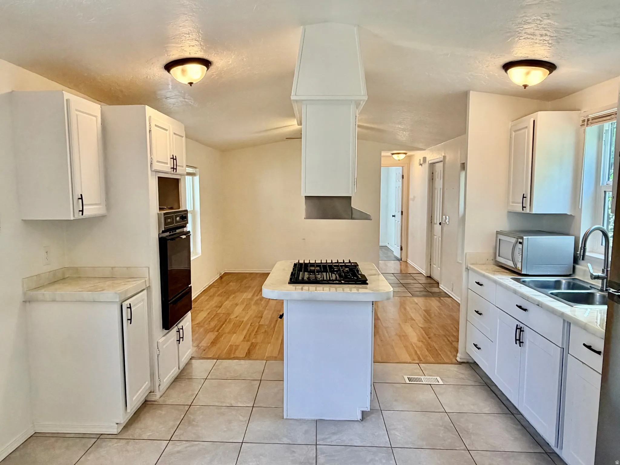 Bright kitchen featuring white cabinetry, a built-in oven, a center island with a gas cooktop and range hood, and tile flooring
