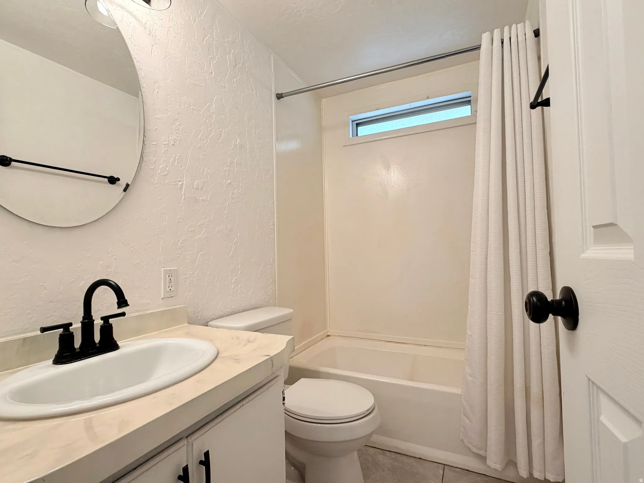 Bathroom featuring a vanity with an integrated sink, matte black faucet, and a circular mirror