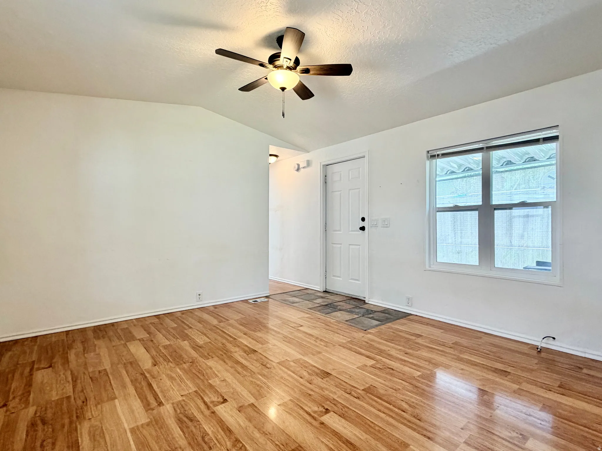 Spacious room featuring wood-finish flooring, a white paneled entry door, and a multi-pane window