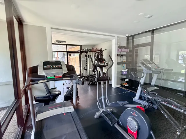 Dedicated fitness space featuring resilient black flooring, bright overhead lighting, expansive glass partitioning, and a large window overlooking outdoor elements