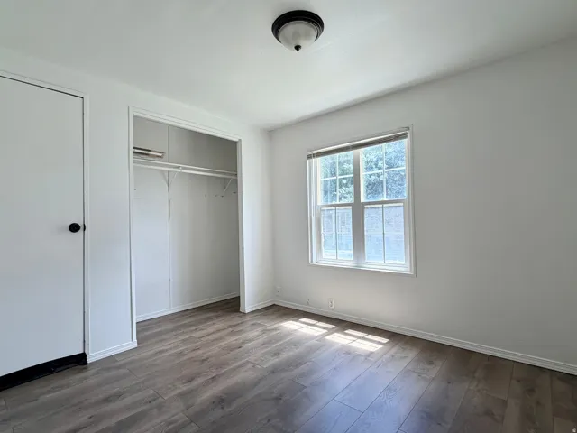 Interior room featuring wood-finish flooring, a double-paned window, and a built-in closet with shelving and hanging rod