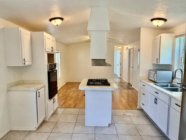 Bright kitchen featuring white cabinetry, a built-in oven, a center island with a gas cooktop and range hood, and tile flooring