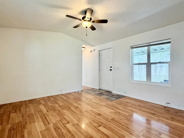 Spacious room featuring wood-finish flooring, a white paneled entry door, and a multi-pane window