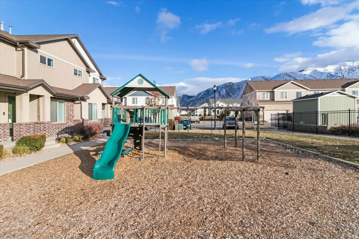 Community playground featuring a playset with a green slide and swing frame on a wood chip surface