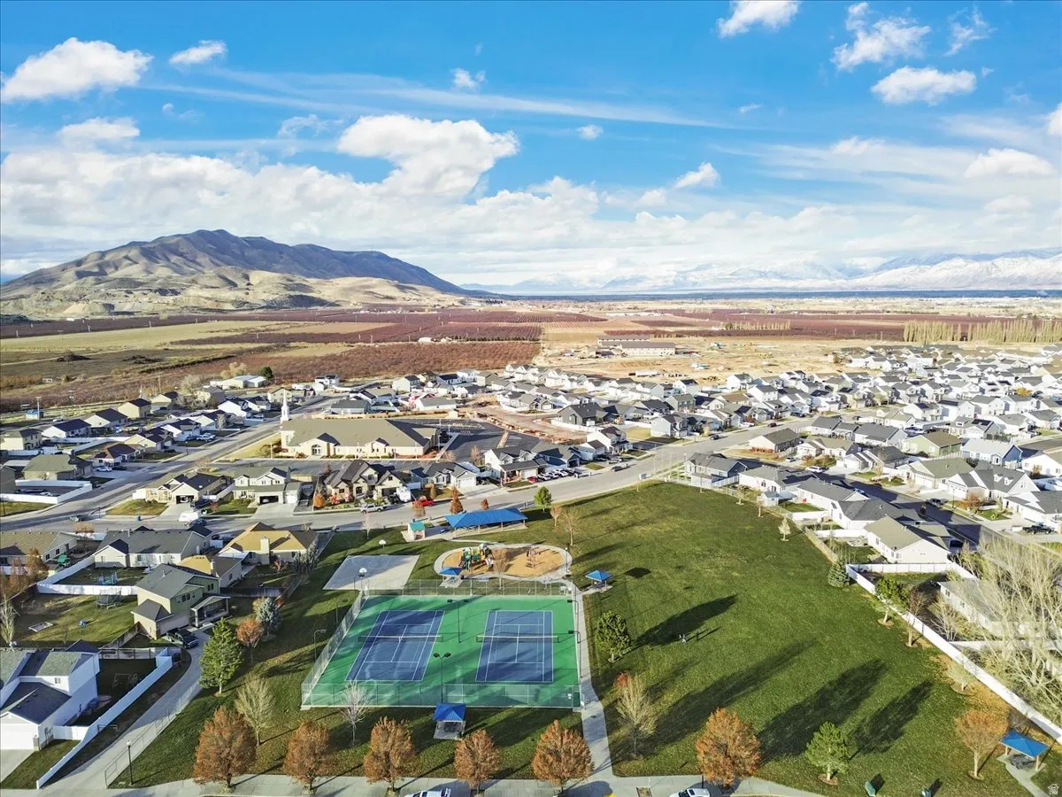 Aerial perspective showcasing a residential community with a large green space featuring a tennis court and playground equipment