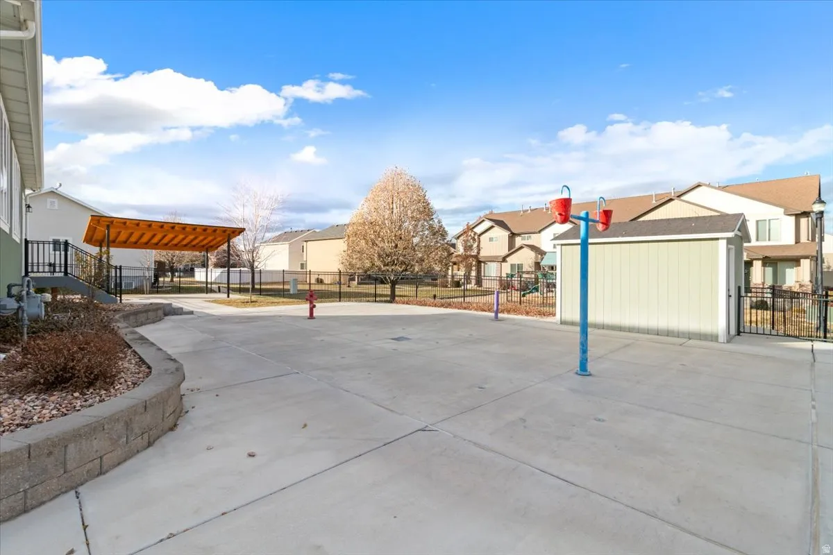 Expansive concrete patio area featuring a slatted wood-finish pergola with a black metal railing