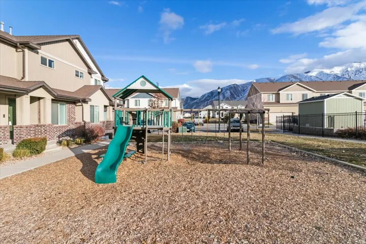 Community playground featuring a playset with a green slide and swing frame on a wood chip surface