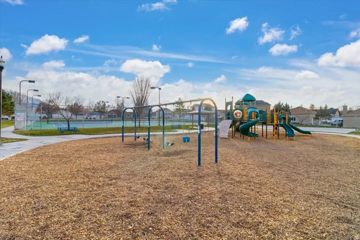 Recreational area featuring a playground with swings and slides, a paved walking path, and a fenced tennis court