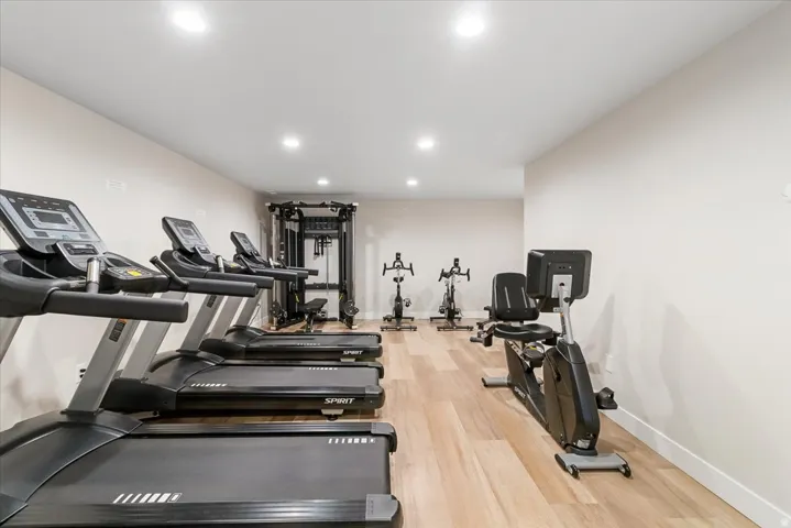 Dedicated fitness area featuring light wood-finish flooring, recessed lighting, and pale neutral walls